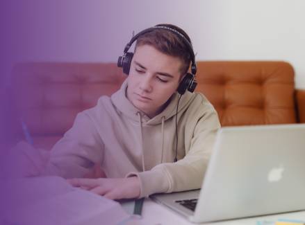 Teenager wearing headphones and writing while using a laptop